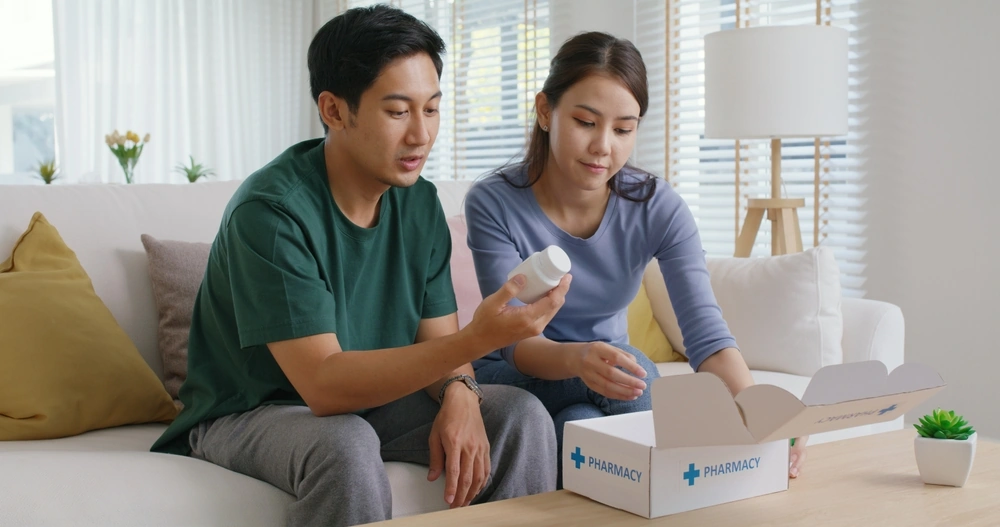 Young married asia people prepare pregnant plan preconception drug at home sofa. Health care unbox open Rx Clomid.